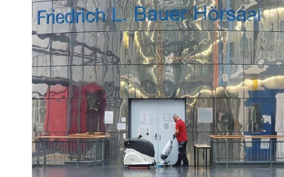 Klüh Reinigungskraft bedient ein Reinigungsroboter vor der Friedrich L. Bauer Hörsaal