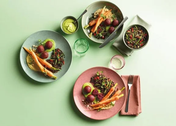 Ein Bild von vier Tellergerichten mit Rote-Bete-Falafeln auf einer grünen Oberfläche