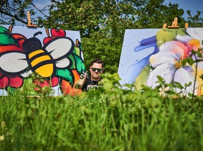 Ein Mann steht zwischen zwei großen Graffiti Gemälden im hohen grünen Gras
