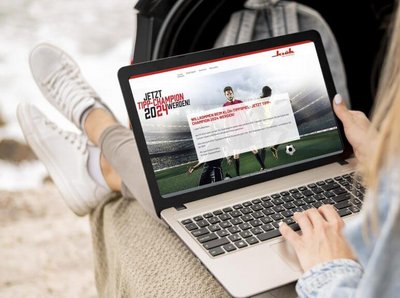 eine Frau hat ein Notebook auf dem Schoss und auf dem Bild ist die Klüh Aktion "Tipp-Champion 2024" zu sehen