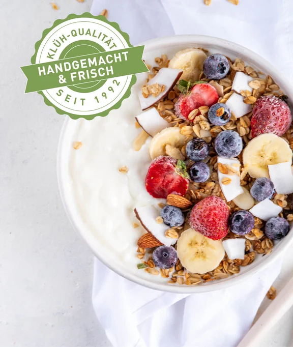 eine Bowl mit Joghurt, Beeren, Nüssen und Kokosnuss und einem "Klüh-Qualität Handgemacht & Frisch seit 1992" Siegel