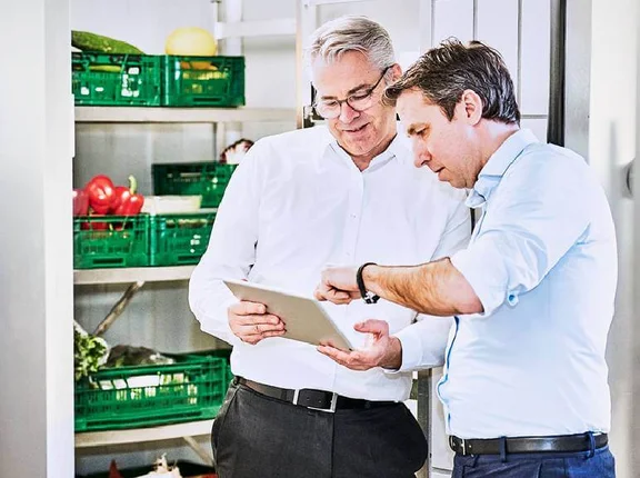 zwei Männer stehen vor einem Gemüse Kühllager und schauen auf ein Tablet