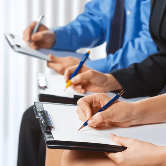 drei Personen mit einem Klemmbrett mit Papier schreiben drauf mit einem Kugelschreiber