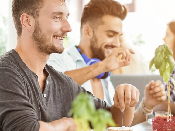 Ein Bannerbild mit Menschen die zusammen am Tisch sitzend essen und trinken. Klüh Catering Logo ist Bild