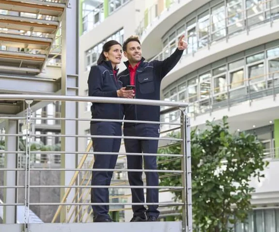 Zwei Sicherheitskräfte stehen auf der Brüstung einer Wendeltreppe und sichten die zu überwachende Umgebung. 