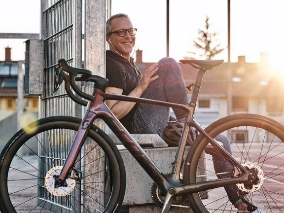 hinter seinem Fahrrad sitzender lächelnder Mann im Sonnenuntergang