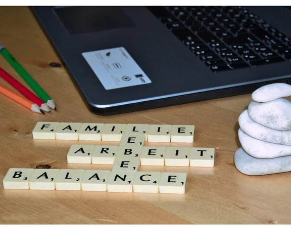 Ein Tisch auf dem ein Laptop, Bleichstifte sind und Scrabbel-Stein ( Spielsteine mit Buchstaben drauf ), welche die Wörte: Familie, Leben, Arbeit, Balance bilden