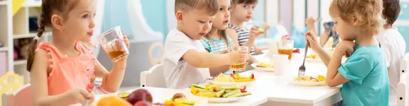 Kindergartenkinder sitzen gemeinsam an einem Tisch und essen.