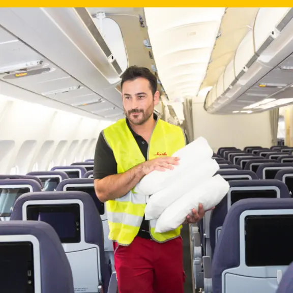 Eine männliche Reinigungskraft läuft durch ein Flugzeug und hält Ersatzhandtücher auf dem Arm.