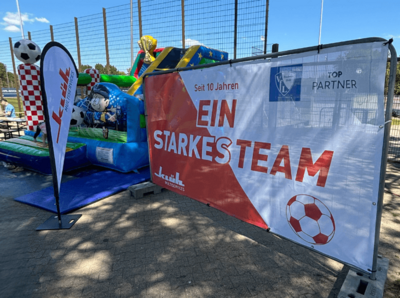Ein Bild von einer Kinder Hüpfburg mit einem Banner von Klüh mit dem Titel " seit 10 Jahren ein Starkes Team" und "TOP PARTNER mit dem VFL Bochum Logo", im Hintergrund sieht man ein Fußball Feld