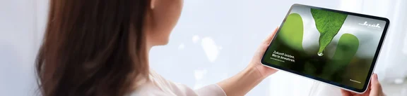 Eine Frau schaut auf ein Tablet, welches sie vor sich hält. Auf dem Tablet ist die Startseite des Klüh-Nachhaltigkeitsbericht 2024 abgebildet.