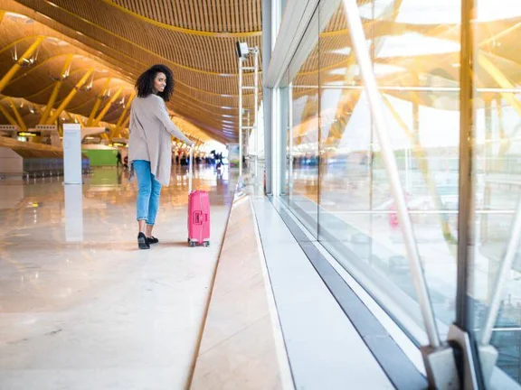 Ein Bild von einer Frau mit einem pinken Reisekoffer im Flughafen Gebäude