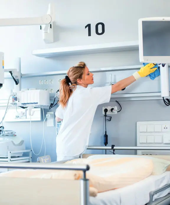 Eine weibliche Reinigungskraft von Klüh reinigt ein Krankenhauszimmer.