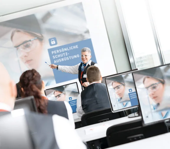 lächelde Frau die auf eine Schulung "Persönliche Schutzausrüstung" zeigt wird aufmerksam von einigen Menschen angehört die an der Schulung teilnehmen