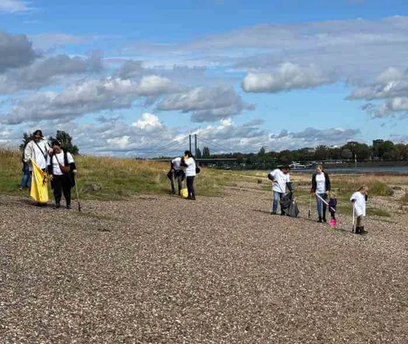 Ein Bild von Menschen, alle tragen weiße T-Shirts und haben Müllsäcke und Müllpicker in der Hand und stehen am Fluss 