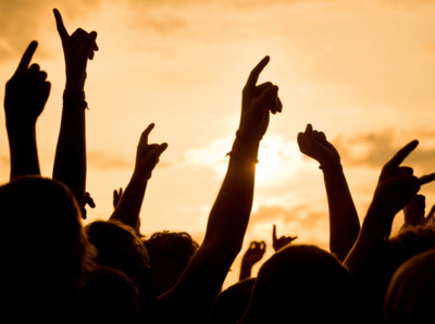 Ein Bild von Menschen die beisamen stehen und die Hände in die Luft strecken im Hintergrund geht die Sonne unter