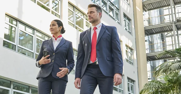 Eine weibliche und eine männliche Sicherheitskraft stehen in einem Gebäude und sichten die zu überwachende Umgebung.