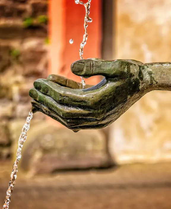 Das Bild zeigt künstliche Hände einer Skulptur, über die Wasser fließt.