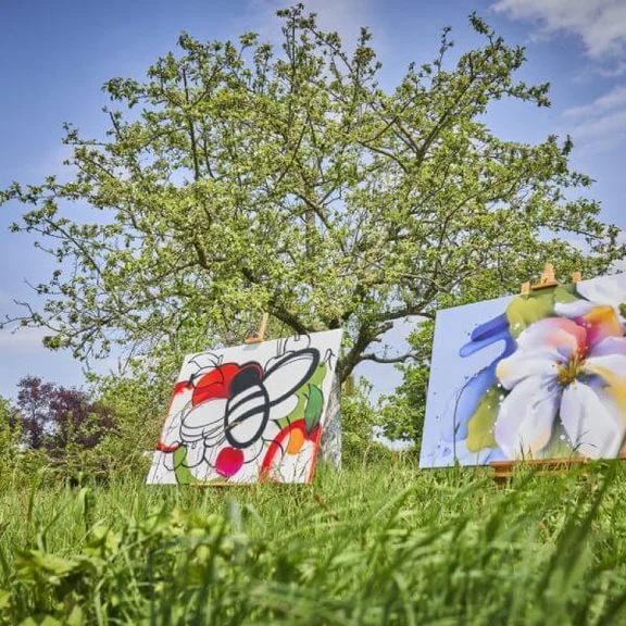 zwei Gemälde aufgestellt auf einer Wiese vor einem Baum 