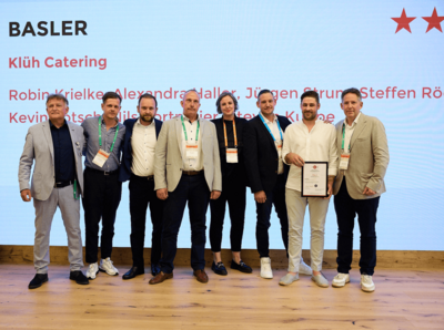 Ein Gruppenbild mit Menschen in Business Outfits die eine Auszeihnung gewonnen haben, im Hintergrund steht an der Wand Klüh Catering