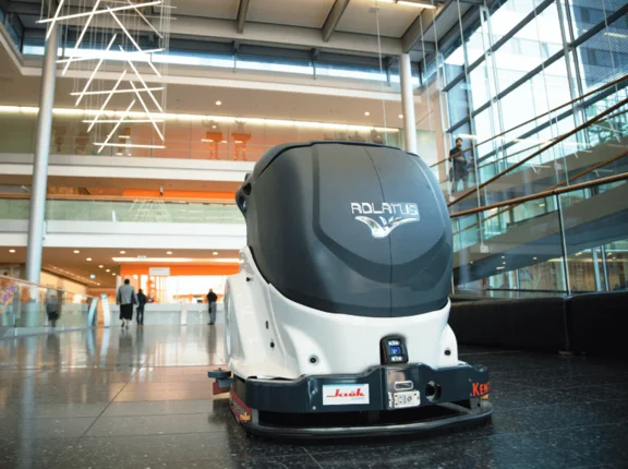 ein Reinigungsroboter mit dem namen "Adlatus" und einem Klüh Cleaning Aufkleber in einem Bürogebäude