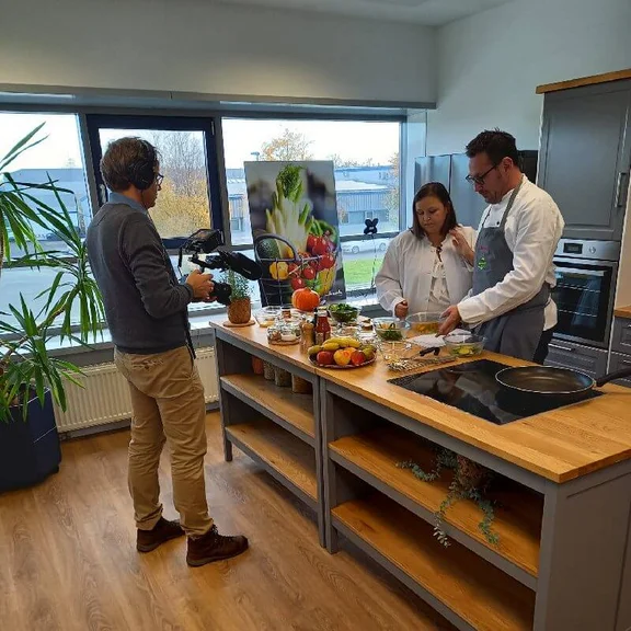 ein Mann und eine Frau kochen in einer Küche und werden dabei von einem Kameramann gefilmt