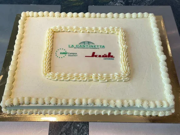 Ein Bild von einer Sahne Torte mit den Logos von EUREF-Campus Düsseldorf, La Cantinetta Betriebsgastronomie und Klüh Catering drauf