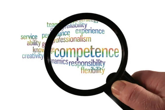 Eine Hand hält eine Lupe über mehrere englische Wörte und vergrößert dabei das Wort "competence"