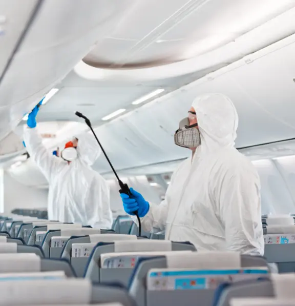 Das Bild zeigt hochspezialisierte Reinigungskräfte mit Sicherheits- und Schutzanzügen, die den Innenraum eines Flugzeuges mit Zerstäubergeräten reinigen.