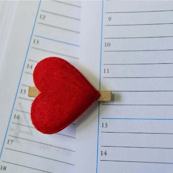 Ein Bild von Wäscheklammer mit einem größeren drauf geklebten roten Herz aus Filz, die Klammer ist an ein Kalnder geklemmt