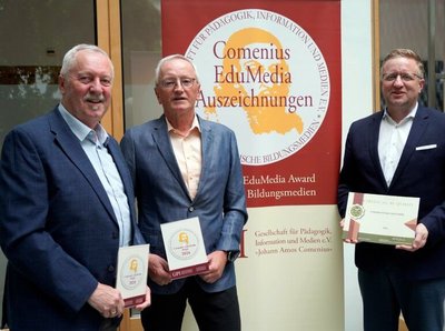 Ein Gruppenbild von 3 Männern in Anzügen, im Hintergrund ist Banner vom Comenius EduMedia Auszeichnungen
