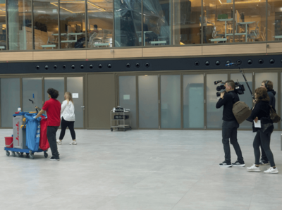 Reinigungskraft auf Reinigungswagen wird von Kamerateam gefilmt