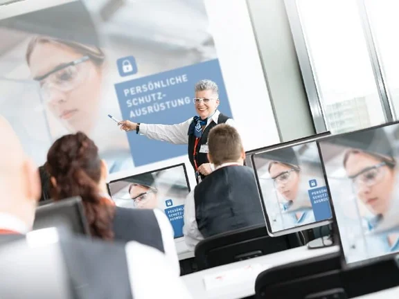 lächelde Frau die auf eine Schulung "Persönliche Schutzausrüstung" zeigt wird aufmerksam von einigen Menschen angehört die an der Schulung teilnehmen
