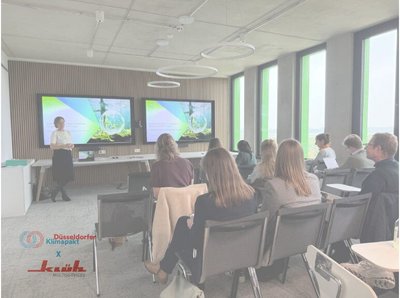 Ein Bild von einem Raum mit 2 Fernsehern worauf viele Menschen sitzend hinschauen, am Rand des Bildes sind die Logos von Klüh Multiservices und Düsseldorfer Klimapakt