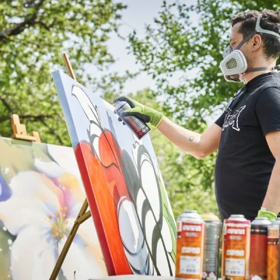 Künstler Damian Bautsch mit Atemschutz beim malen eines Gemäldes mit Graffiti-Sprühdosen in freier Natur