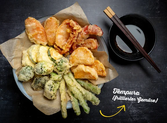 Ein Bild von einem Teller mit Tempura (frittiertem Gemüse) und eine Schale mit einer Soße und als Besteck Essstäbchen