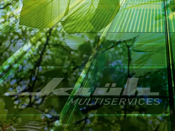 Das Bild zeigt grüne Bäume und Blätter, die sich in der Außenfassage des Klüh Firmengebäudes spiegeln.
