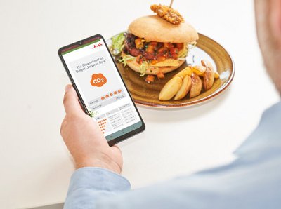 ein Mann schaut sich die Gericht details seines Burgers in der Klüh Catering App an 