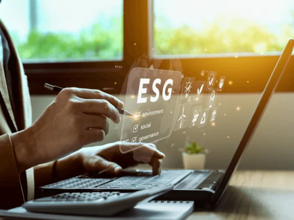 Ein Bild von Person am Schreibtisch, vor ihr ist ein Notebook, Notizblock und Taschenrechner zudem sind visuelle elemente mittig im Bild mit Icons mit dem Titel ESG