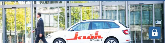 Ein Mann im Anzug läuft an einem Auto vorbei, dass den Schriftzug Klüh Security auf der Seite hat.