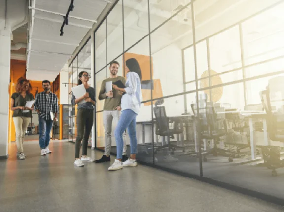 5 Menschen mit Papierblättern in den Händen im Flur eines Bürogebäudes die sich unterhalten