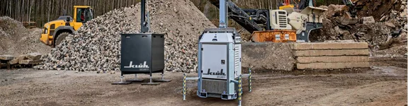 Ein Bild auf einer Baustelle, im Vordergrund sind zwei Klüh Security Tower, im Hintergrund sind zwei Bagger und Schuttberge