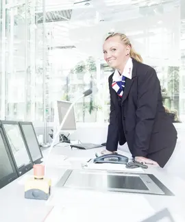 Eine weibliche Servicekraft steht lächelnd an einem Arbeitsplatz mit mehreren Bildschirmen.