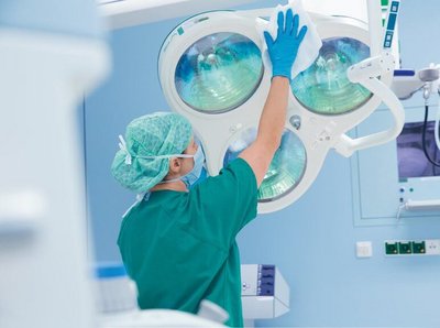 eine Person in OP-Kleidung reinigt mit einem Tuch OP-Geräte