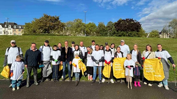 Ein Gruppenbild von vielen Menschen in weißen Klüh T-Shirts mit Müllsäcken und Müllpickern in den Händen