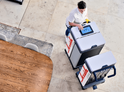Reinigungskraft steht mit einem Reinigungswagen mit Tablet neben einem Konferenztisch