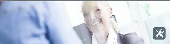 Eine lächelnde Frau sitzt und trägt ein Hemd mit einem roten Klüh Logo und schaut auf die Person vor sich