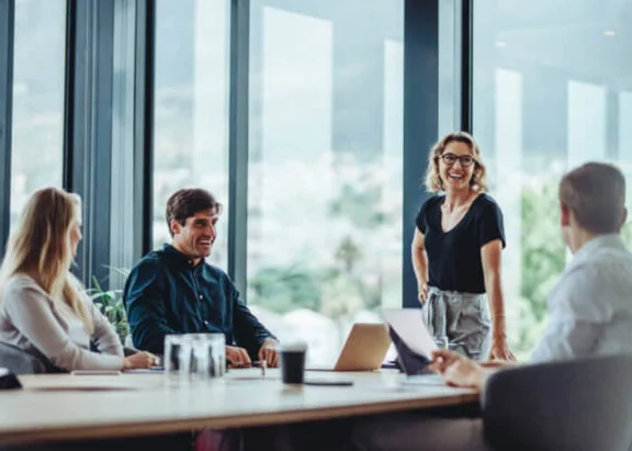 Ein Bild von zwei Männern und zwei Frauen in einem Besprechungsraum, alle lächeln und schauen sich gegenseitig an