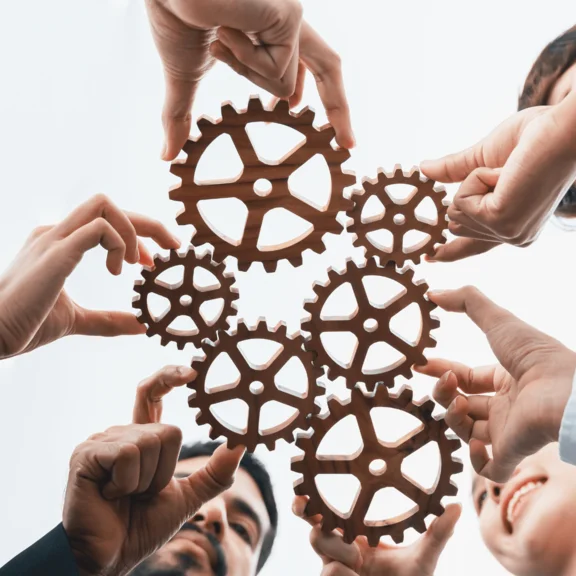 Ein Bild von mehreren Holz Zahnrädern die in einander sitzen und von jeweils einer Person gehalten werden