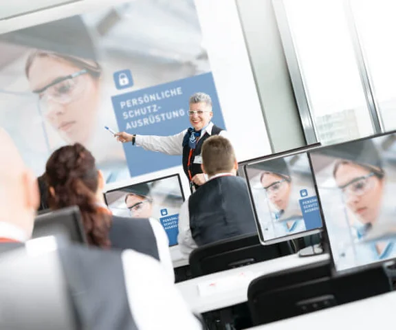 lächelde Frau die auf eine Schulung "Persönliche Schutzausrüstung" zeigt wird aufmerksam von einigen Menschen angehört die an der Schulung teilnehmen